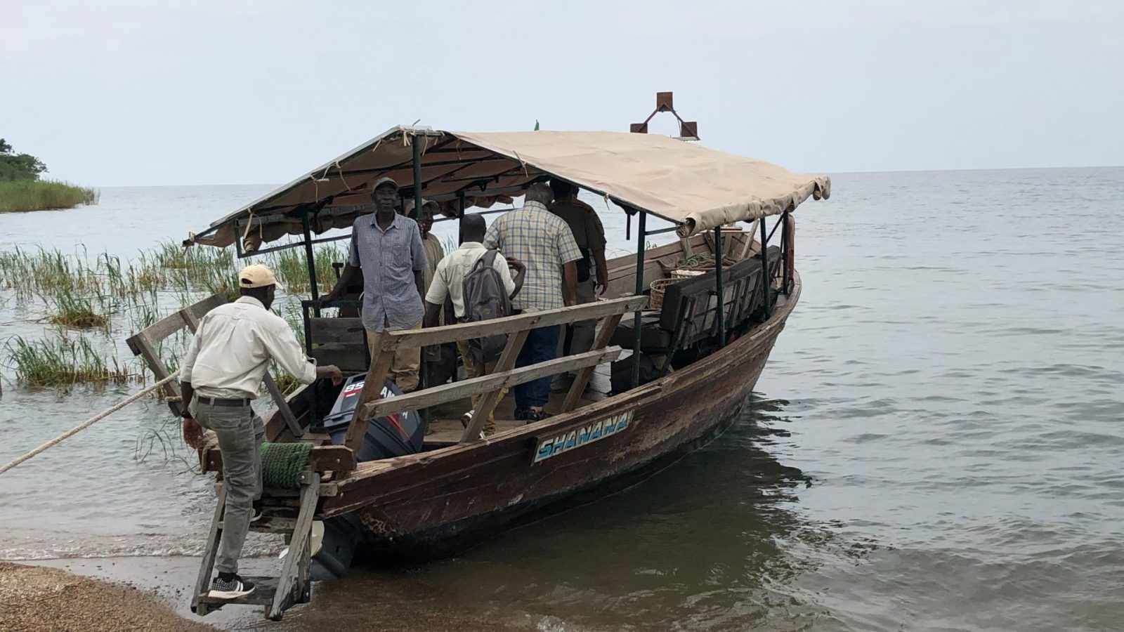 Passengers boarding a canvas-roofed wooden boat beached on the lakeshore