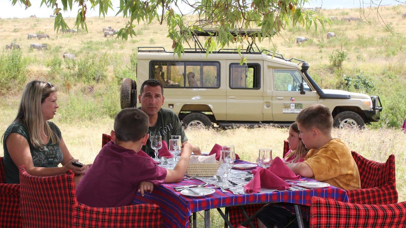 A family bush lunch laid out on a table beside a safari vehicle