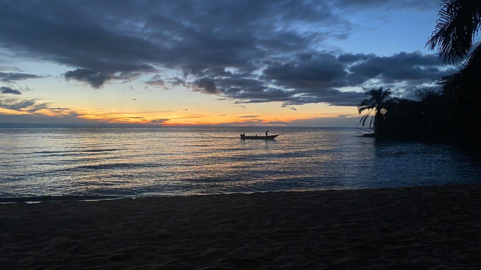A fishing boat silhouetted against an orange dusk horizon on the lake