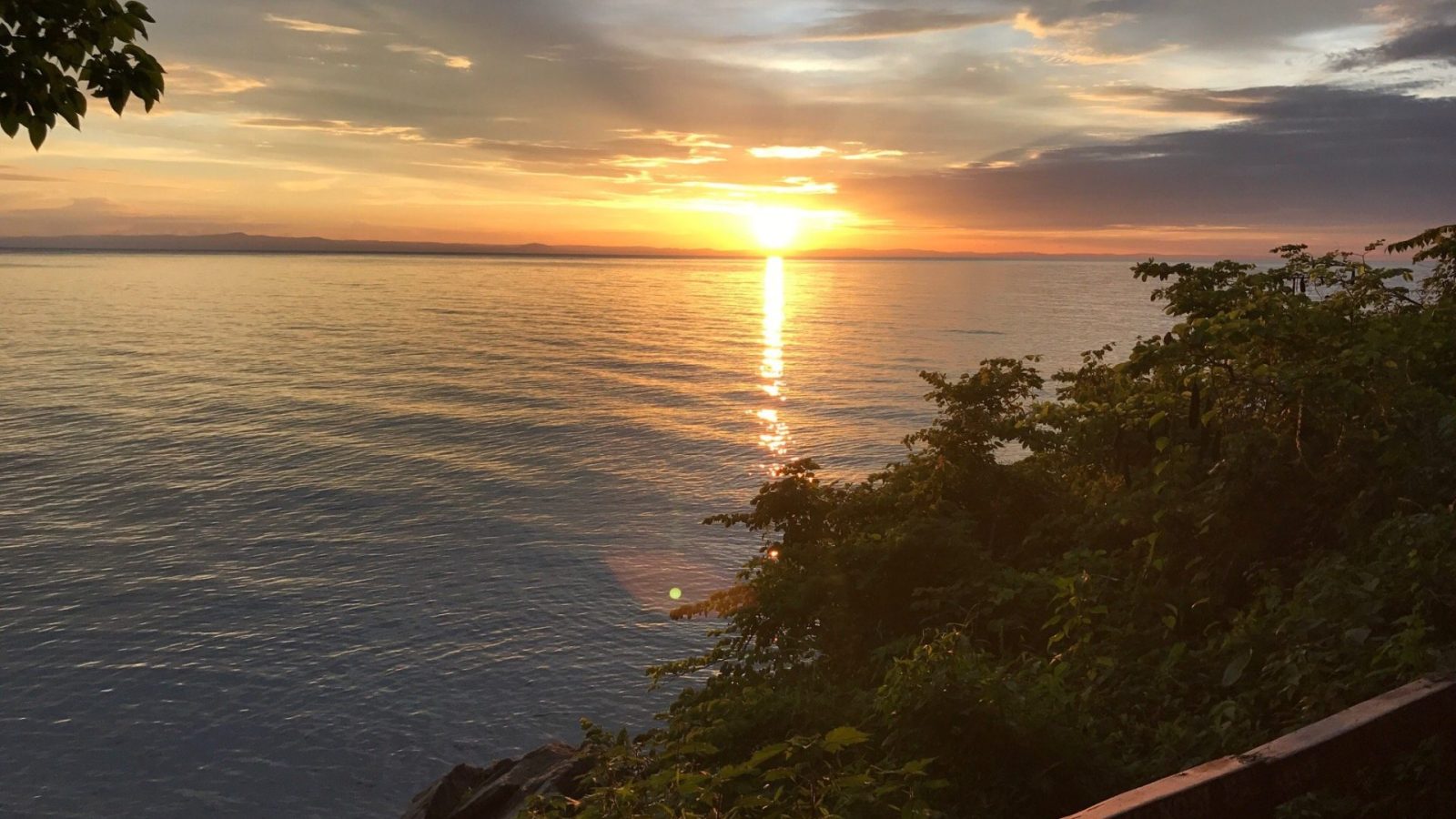 A golden sunset over the lake seen past a wooden deck railing
