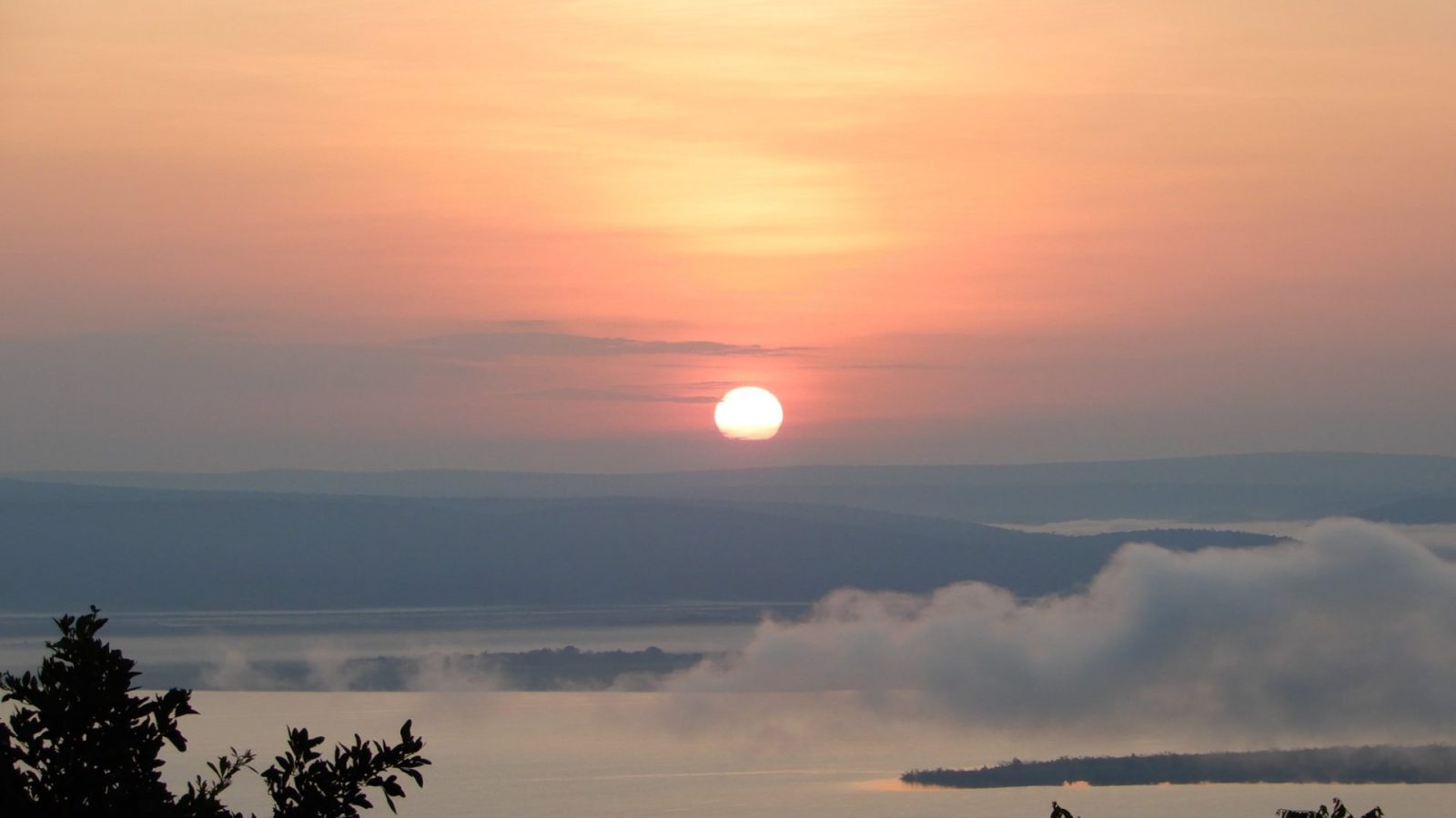 An orange sunrise over a still lake backed by low hills