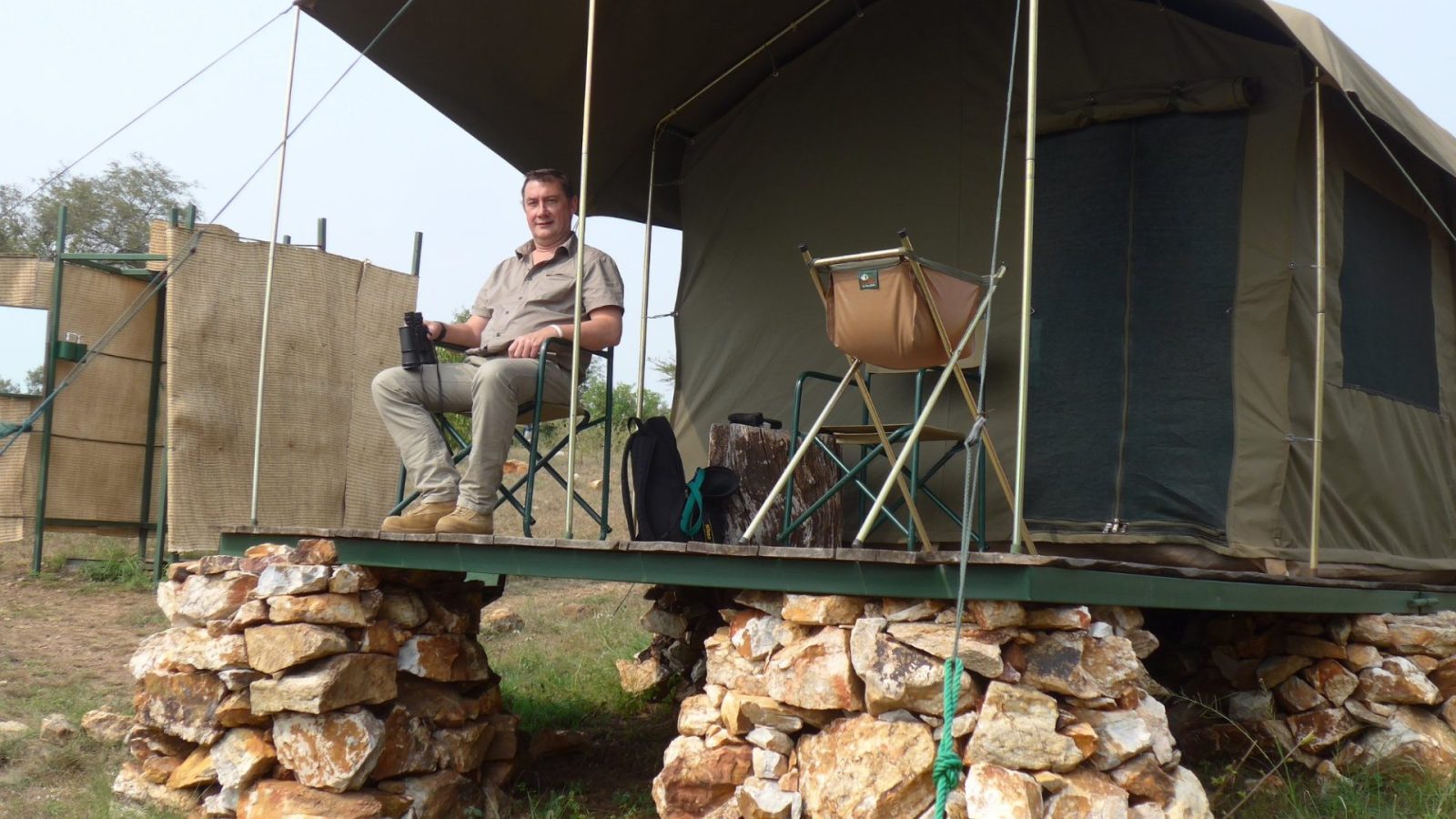 A guest on the deck of a safari tent looking out over the bush with binoculars