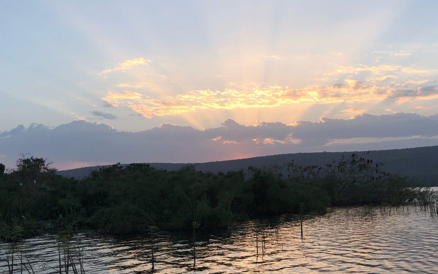 Sun rays breaking through cloud over a lake at sunset
