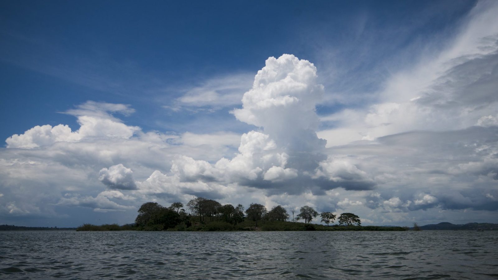 A low wooded island on Lake Victoria beneath towering white cloud